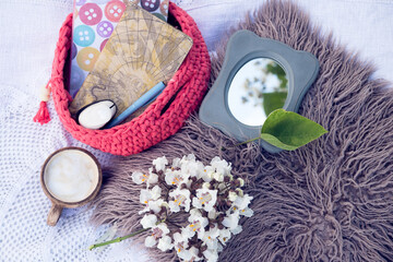 Layout of crochet bascket with paper notebooks, liner and punch together with a mirror with leaves reflection, cup of coffee and acacia flower, all on a fluffy pillow and crochet texture.