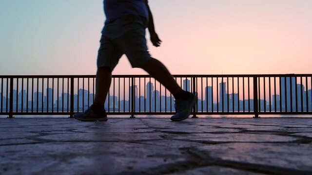 Slow-Motion, Silhouette: A man exercising-walking with a city skyline in the background during sunrise in Sharjah, United Arab Emirates