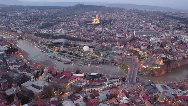 Aerial panoramic view of illuminated historic center of Tbilisi city on banks of Mtkvari River on spring twilight, Georgia