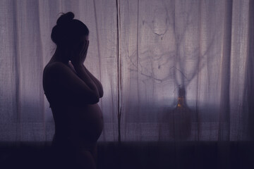 Young pregnant woman crying with her hands folded near her face. Pregnancy problems, silhouette of...