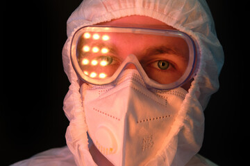 Doctor in white medical suit with protective goggles with reflective light of lamps, face close up