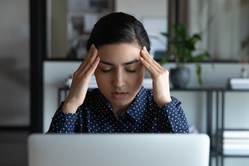 Tired young Indian woman work on computer massage temples suffer from headache migraine overwork on...