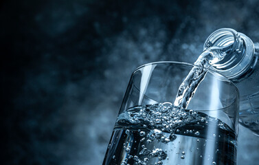 Pouring water from bottle into glass on black background