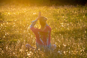 Woman is meditating at sunset in a field during golden hour