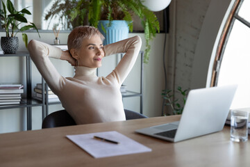 Happy Caucasian businesswoman relax in chair at desk in office distracted from computer work...