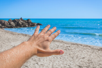 The young man stretched his hand forward to the sea and sky on the beach. The concept of freedom and rest at sea