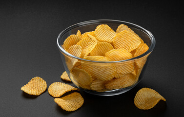 Ridged potato chips in glass bowl on black background