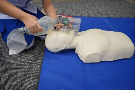 A medical professional demonstrates CPR on a dummy using a bag valve mask, emphasizing emergency response training and life-saving techniques.