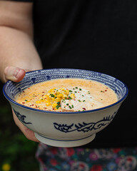 Holding bowl of cheese ramen noodle soup with corn