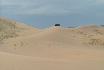 the car stands on top of a high dune in the desert