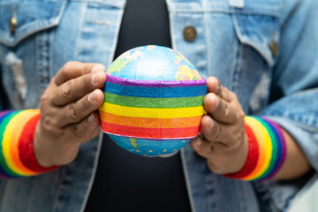 Asian lady holding rainbow color flag with globe, symbol of LGBT pride month celebrate annual in...
