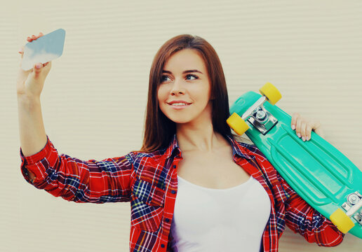 Portrait of young woman taking a selfie picture by smartphone with skateboard on a white background