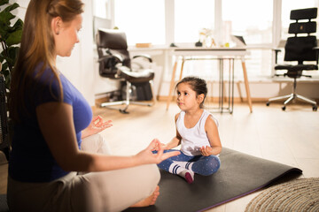 Woman in casual clothes meditating with her daughter and sitting on lotus pose