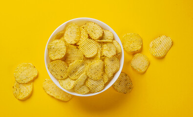 Ridged potato chips in bowl on yellow background