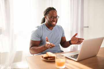 Fototapeta na wymiar Handsome young multiracial man with dreadlocks working with laptop at the kitchen
