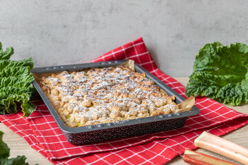 Kuchen mit Rhabarber und Streusel aus einem Blech auf einem Tisch aus hellem Holz
