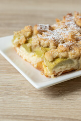 Kuchen mit Rhabarber und Streusel aus einem Blech auf einem Tisch aus hellem Holz