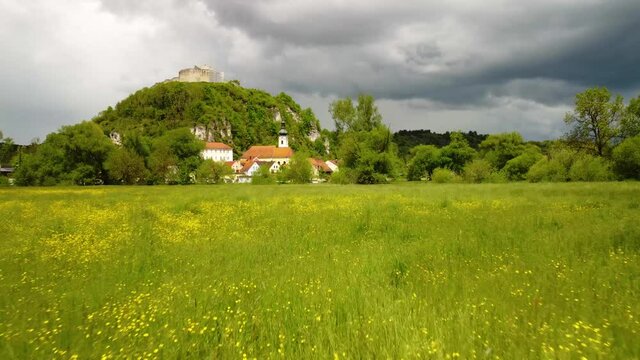 Drone flying very low over blooming summer meadow towards Kallm&uuml;nz, Bavaria on sunny day with dramatic clouds