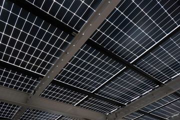 Solar energy panels installed on steel beams to cover a car park, seen from below. Sustainable energy and shade at the same time