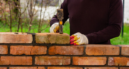 a man builds a brick wall, puts a brick on a cement-sand mortar, tapping a brick with a hammer