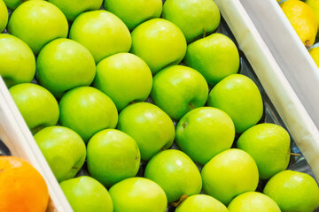 Fresh bright green apples are arranged neatly in a row in a box on the market in the supermarket counter.