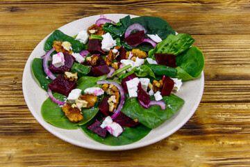Tasty spinach salad with boiled beetroot, feta cheese, walnut and red onion on wooden table. Healthy vegetarian food