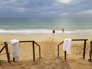 A couple of elderly people go to swim in the sea in the morning against the backdrop of a gloomy sky