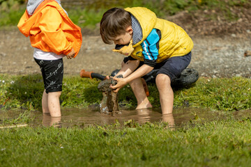 Children playing in the puddle lifting a rock from the water