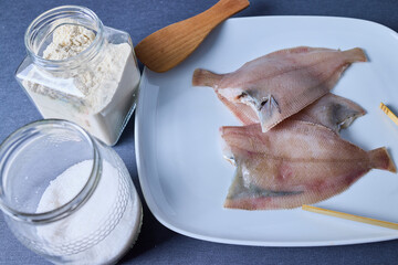 Several sole on a plate and two jars with salt and flour