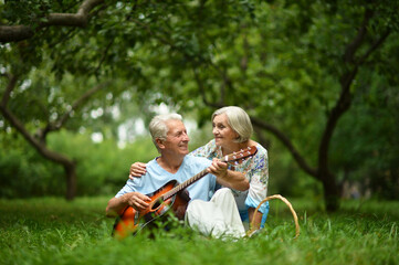 Naklejka na ściany i meble Happy senior couple on picnic. man playing guitar