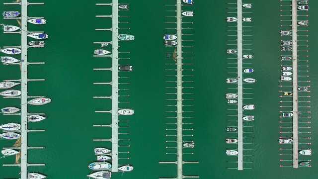 Aerial top view of a lot of white yachts and sailboats moored in marina on a turquoise water, spring season