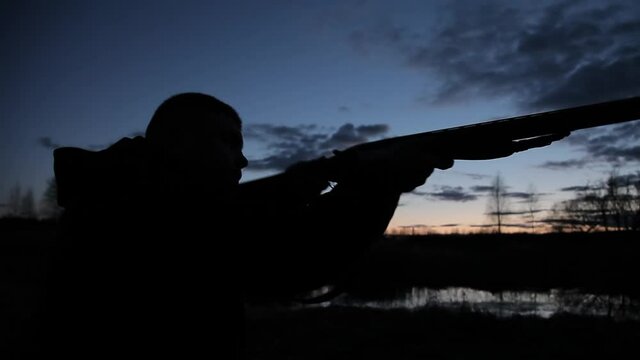 Silhouette of a hunter at night with a gun. Silhouette of a hunter with a gun on a sunset background. A man with a gun on the background of the evening sky and the river on the hunt