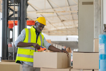 Black male workers wear yellow helmet safety packing cargo into boxes to prepare for shipping at warehouse factory.