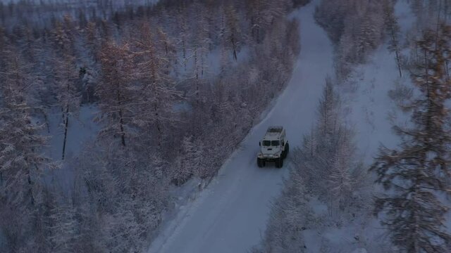 The six-wheel Trekol all-terrain vehicle rides through the snow-covered tundra in the sunset light
