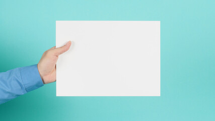 Hand is holding blank A4 paper and wear blue long sleeve shirt on green mint or Tiffany Blue background.