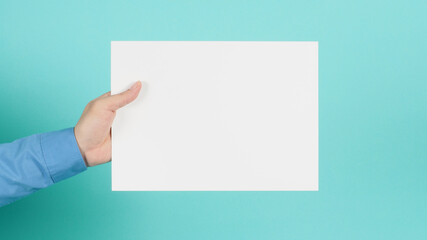 Fototapeta premium Hand is holding blank A4 paper and wear blue long sleeve shirt on green mint or Tiffany Blue background.