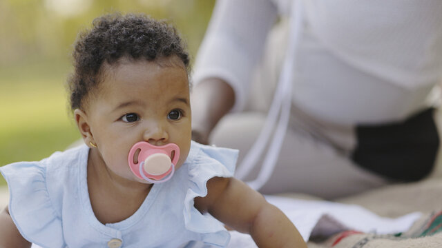 African American Baby Is Sucking Pacifier Happy With Family In Garden. Love Caring For Children From Mother. Development Of Young Children In Vision. Good Health Of Children