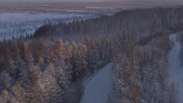 The six-wheel Trekol all-terrain vehicle rides through the snow-covered tundra in the sunset light
