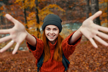 happy woman with a backpack travels in the park in autumn and gesticulate with the hands of the...