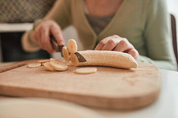 Young girl chopping with the knife fresh banana while baking bagels at the kitchen