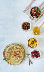 Folded thin pancakes strawberry slices, raspberries, green tea, honey on a gray background