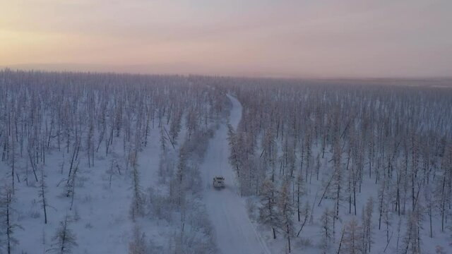 The six-wheel Trekol all-terrain vehicle rides through the snow-covered tundra in the sunset light
