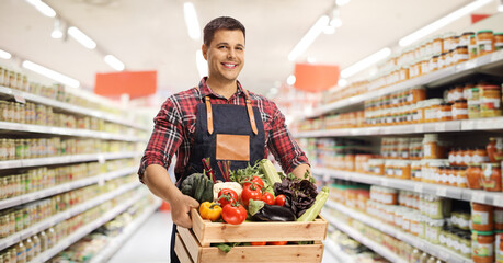 Young man carrying a crate with fresh vegetables in a supermarket