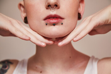 Woman with piercing at her face and ear tunnels posing with hands near her face - 434790241