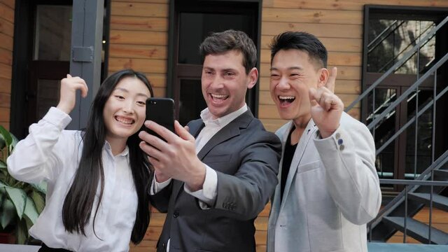 Three multinational asian business people laughing smiling talking communicating making selfie photos using mobile phone app in meeting room or restaurant record lifestyle blog.