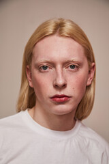 Naklejka premium Albino feminine man posing in studio dressed in white t-shirt isolated on a beige