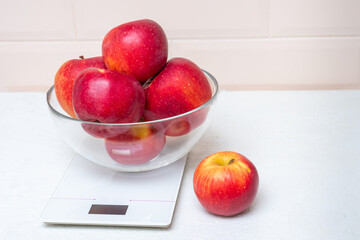 Red apples in a transparent bowl on a kitchen scale, copy space, close-up. The concept of healthy eating