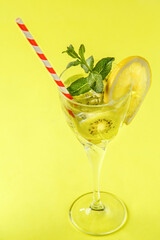 Kiwi cocktail decorated with lemon and mint in a glass on a napkin on a yellow background.