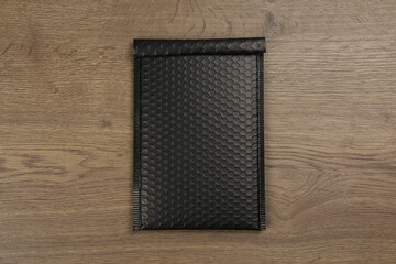 Black padded envelope with bubble wrap on wooden background, top view