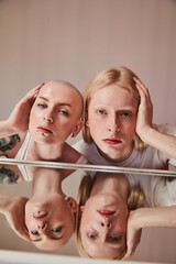 Albino man and bald woman with piercing at her face looking reflected at the table